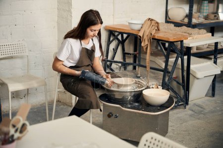 Foto de Mujer trabajando en rueda de cerámica en taller haciendo tazón de barro en estudio de cerámica - Imagen libre de derechos