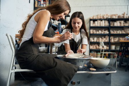 Téléchargez les photos : Artiste céramique féminine travaillant avec la roue de poterie fabrication de plaque artisanale dans l'atelier de poterie - en image libre de droit