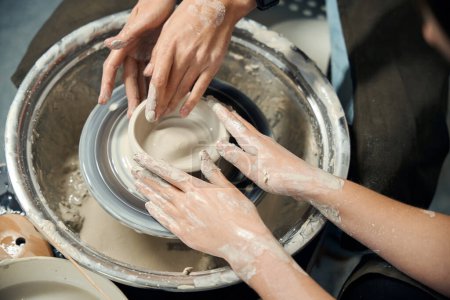 Foto de Mujeres irreconocibles haciendo jarra de arcilla escultura en taller sobre rueda de alfarero en estudio de cerámica - Imagen libre de derechos