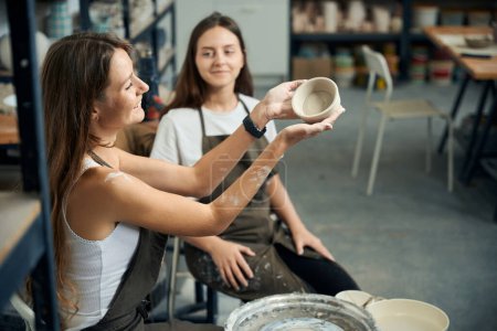 Photo for Women ceramics workers admiring beautiful clay dishes in creative studio - Royalty Free Image