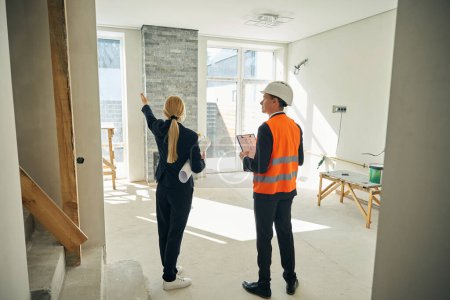 Photo for Back view photo of construction manager standing in room near client woman who pointing at something with her hand - Royalty Free Image