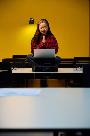 Téléchargez les photos : Jeune asiatique inquiète employée informatique avec des mains priantes regardant ordinateur portable assis sur le bureau dans le bureau de coworking. Concept de travail indépendant ou à distance moderne - en image libre de droit