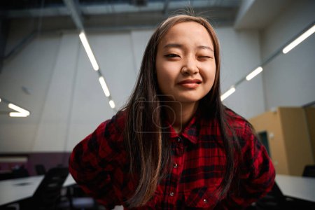 Téléchargez les photos : Jeune asiatique employée informatique clin d'oeil à la caméra pendant la pause dans le bureau de coworking. Concept de travail indépendant ou à distance moderne - en image libre de droit