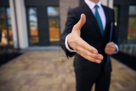 Téléchargez les photos : Photo recadrée de la main d'un homme d'affaires, qui la donne pour une poignée de main tout en se tenant près du bâtiment - en image libre de droit