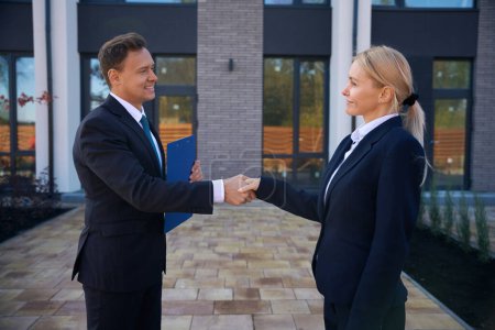Photo for Satisfied male and female business partners in suits standing near office and shaking hands - Royalty Free Image