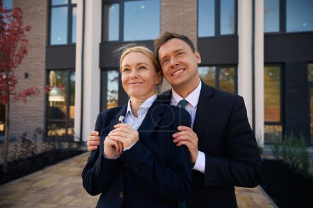 Photo for Close up picture of satisfied man standing and embracing joyful woman who holding keys in her hands - Royalty Free Image
