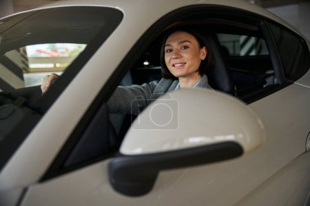 Foto de Retrato de una hermosa mujer joven en un coche nuevo mirando en el espejo retrovisor y sonriendo - Imagen libre de derechos
