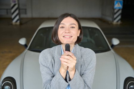 Téléchargez les photos : Portrait de femme assise sur une voiture neuve, souriante et tenant des clés. Concept d'achat de transport - en image libre de droit