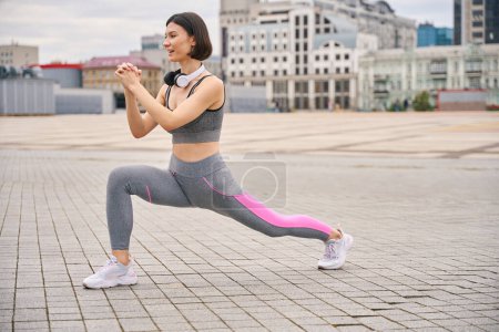 Photo for Young lady in sporty clothes with headphones does warm-up for legs. Concept of healthy lifestyle - Royalty Free Image