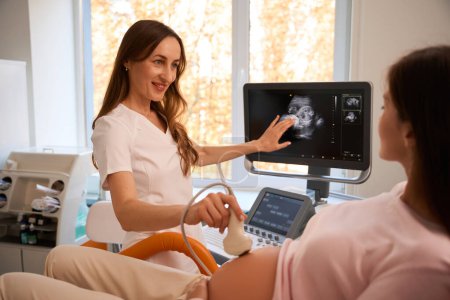 Foto de Médico haciendo ultrasonido procedimiento de ecografía a la mujer embarazada transductor en movimiento en el vientre de la futura madre - Imagen libre de derechos