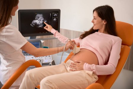 Téléchargez les photos : Médecin utilisant un équipement d'échographie pour examiner la femme enceinte à l'hôpital - en image libre de droit