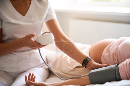 Foto de Médico femenino irreconocible que revisa la presión arterial de la mujer embarazada durante el embarazo en el hospital - Imagen libre de derechos