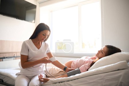 Médecin prenant des femmes enceintes pression artérielle avec sphygmomanomètre à la maternité
