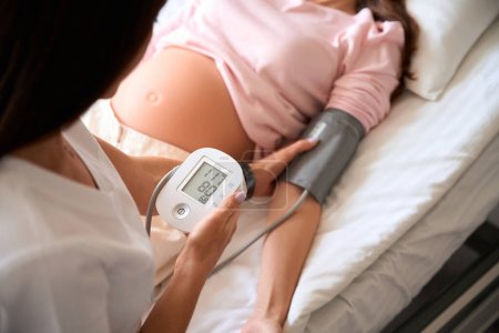 Foto de Médico irreconocible tomando mujeres embarazadas presión arterial en la clínica de maternidad - Imagen libre de derechos