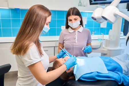 Foto de Asistente dental ayuda en la cita, médico trata diente de paciente joven - Imagen libre de derechos