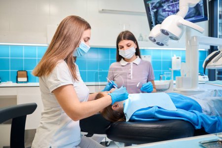 Foto de Asistente ayuda a un dentista en una cita, un médico trata un diente a un paciente joven - Imagen libre de derechos