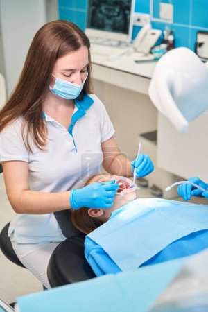 Téléchargez les photos : Adolescent dans une chaise de dentiste confortable, le personnel médical utilise des instruments dentaires spéciaux au travail - en image libre de droit