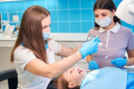 Téléchargez les photos : Médecin et un assistant effectuer des procédures dentaires sur une fille, en utilisant des instruments spéciaux - en image libre de droit