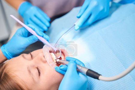 Téléchargez les photos : Dentiste perce une dent dans une adolescente, un assistant tient un éjecteur de salive - en image libre de droit
