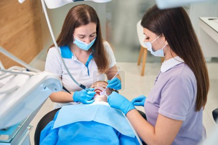 Young woman dentist with an assistant treats the teeth of a teenage girl, using modern equipment