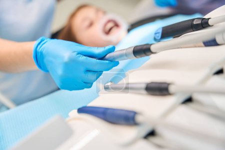Foto de Dentista femenina en el lugar de trabajo utiliza accesorios estériles para un taladro, médico con guantes de protección - Imagen libre de derechos