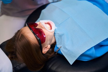 Adolescente se trouve dans une chaise dentaire, portant un rétracteur dentaire et des lunettes de protection