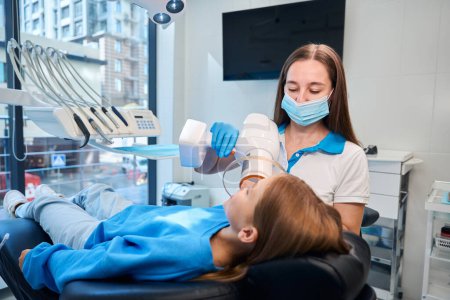 Photo for Dentist holds a photopolymer lamp in his hands, a teenage girl is at her appointment - Royalty Free Image