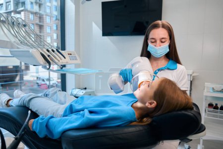 Femme dentiste tient une lampe photopolymère dans ses mains alors qu'elle voit une adolescente