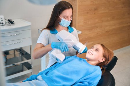 Dentist uses a modern photopolymer lamp at work, she is seeing a teenage girl