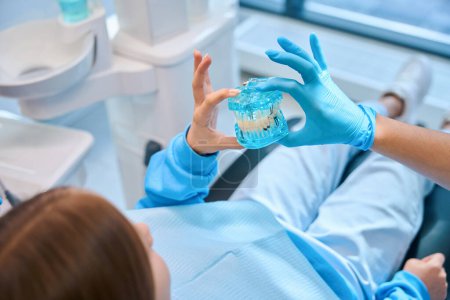 Foto de Mujer dentista sostiene un modelo de la dentición en sus manos, ella aconseja a una adolescente - Imagen libre de derechos