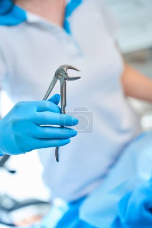 Zahnarzt in Schutzhandschuhen hält ein Werkzeug zur Zahnentfernung in der Hand, ein Arzt in Uniform