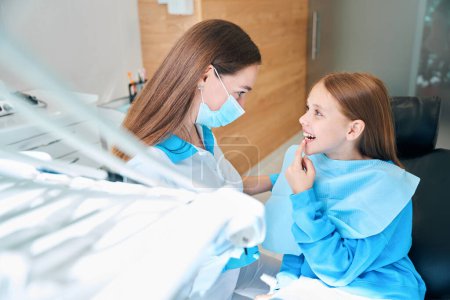 Foto de Chica muestra sus dientes al dentista con un higienista, un médico con una máscara protectora y guantes - Imagen libre de derechos