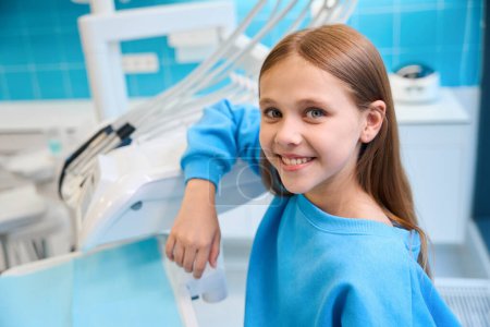 Smiling girl is in a dental office, wearing a blue sweatshirt