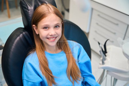 Foto de Una paciente joven está sentada en una silla dental, con una sudadera azul - Imagen libre de derechos