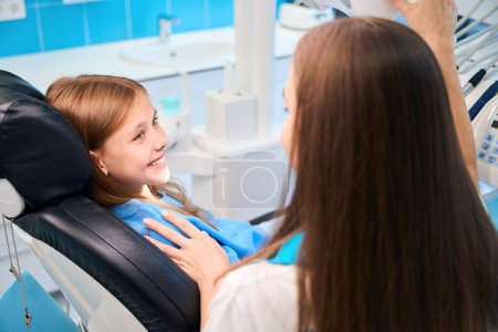 Foto de Chica sonriente se comunica con una doctora en un consultorio dental, en el interior con equipos modernos - Imagen libre de derechos