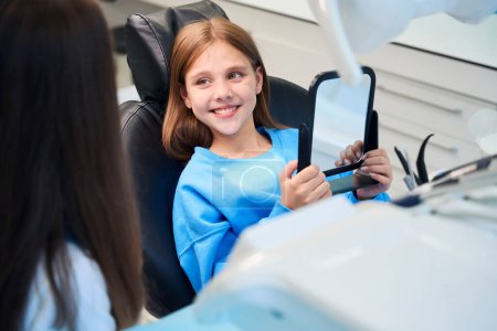 Foto de Joven paciente admira su sonrisa de dientes blancos en el espejo, junto a una dentista - Imagen libre de derechos