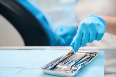 Dentist hygienist at workplace uses sterile instruments, woman wearing protective gloves