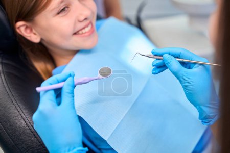 Foto de Sonriente adolescente se sienta en la silla de dentistas, el especialista comienza a examinar los dientes de las niñas - Imagen libre de derechos