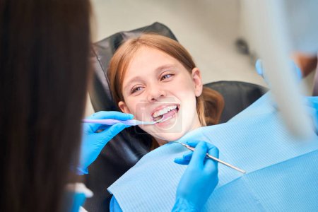 Lächelndes Mädchen im Zahnarztstuhl, der Arzt untersucht ihre Mundhöhle