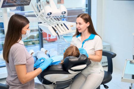 Foto de El personal de la clínica está realizando una cita en un consultorio dental, una paciente joven está sentada en una silla - Imagen libre de derechos