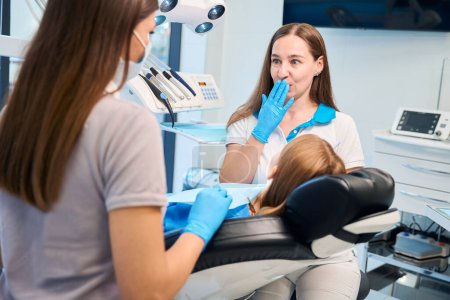 Foto de Joven dentista y asistente están llevando a cabo una cita en un consultorio dental, una paciente joven está sentada en una silla - Imagen libre de derechos