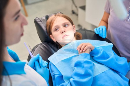 Foto de Los médicos están llevando a cabo una cita en un consultorio dental, una paciente asustada niña está sentada en una silla - Imagen libre de derechos