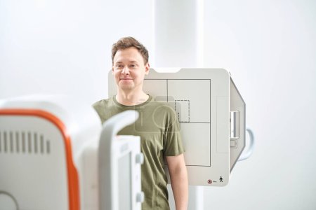 Mann lehnt sich aufrecht mit dem Rücken an Bildrezeptor vor Röntgengerät
