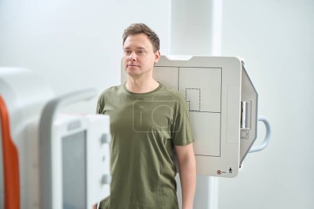 Foto de Retrato de la cintura hacia arriba del paciente apoyando su espalda contra el receptor de imagen frente a la máquina de radiografía - Imagen libre de derechos