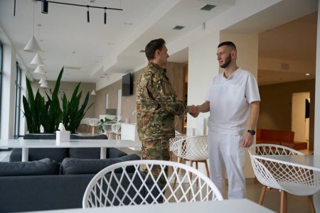 Doctor shaking hands with serviceman while standing in waiting area of medical facility