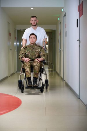Portrait grandeur nature d'une infirmière poussant un fauteuil roulant avec un militaire le long du couloir de l'hôpital