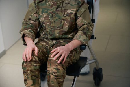 Zugeschnittenes Foto von medizinischem Personal, das Rollstuhl mit Militärmann auf dem Korridor medizinischer Einrichtungen schiebt