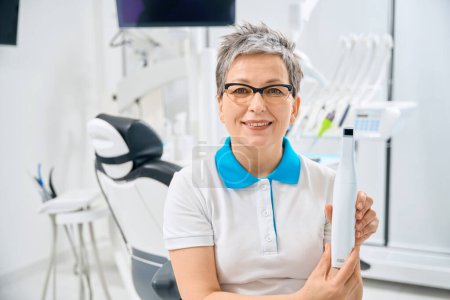 Smiling woman dental therapist holding in hands and showing portable dental scanner, modern tool to examine each tooth of patient and find all possible diseases, aesthetic dentistry