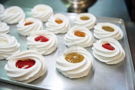 Photo for View to many fresh and crispy merengue nests filled with fresh and sweet fruit curd mousse, food preparation for mini Pavlova dessert, professional bakery - Royalty Free Image