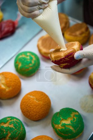 Großaufnahme Bäckerin füllt Choux au Craquelin mit Kondensmilch, Karamellcreme oder Pudding und bereitet süßes und schmackhaftes Dessert zu